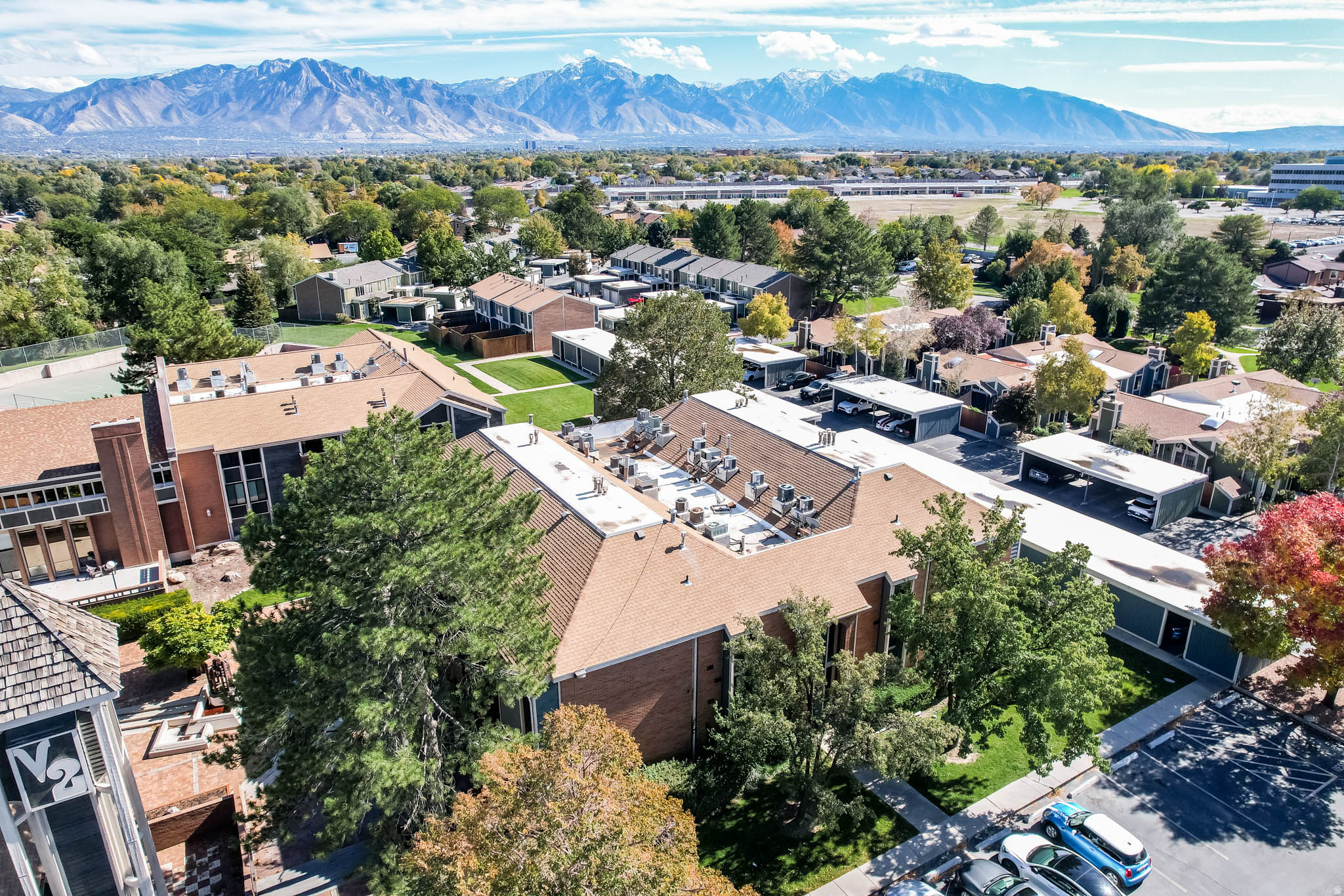 Expansive property featuring multiple buildings with pitched roofs, mature trees, manicured green spaces, and mountain scenery