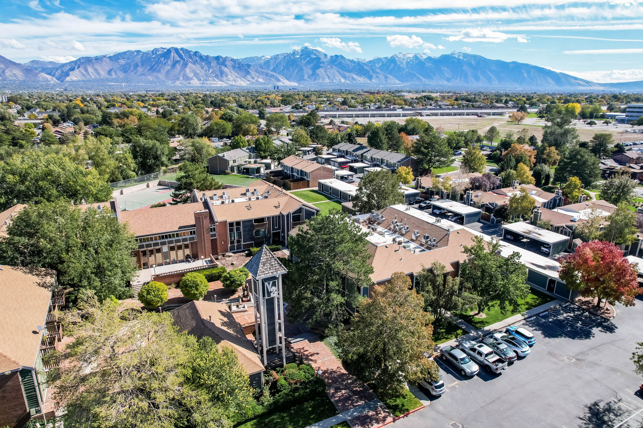 Expansive property featuring multiple residential buildings with red-toned roofs, a distinctive bell tower, a tennis court, and covered parking structures