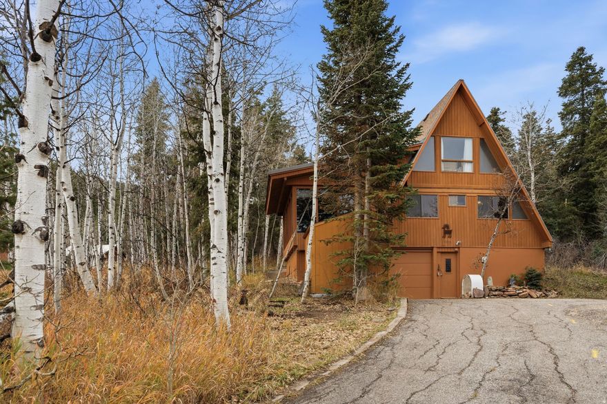 Nestled among aspen and evergreen trees, this charming 2-bedroom, 1-bath A-frame cabin offers a peaceful mountain retreat on a  acre lot.   With 1,658 square feet of living space, the home combines rustic character with a timeless alpine feel. The open concept living area features vaulted wood paneled ceilings, expansive windows, and warm natural light that fills the space. The adjacent kitchen retains its original charm with practical cabinetry and tile flooring, maintaining the cabin's cozy, authentic atmosphere. Two bedrooms are conveniently located on the main level, with a spacious loft area above that serves perfectly as a flex space: ideal for a bedroom, an office, or guest area. A bright sunroom with panoramic forest views provides the perfect spot to enjoy the quiet setting year-round. Outside, the property's  acre wooded lot offers privacy, surrounded by quaking aspens, evergreens, and native mountain vegetation. The attached garage provides additional storage and easy access in all seasons. Whether used as a year-round residence or a weekend getaway, this inviting A-frame cabin captures the beauty and serenity of mountain living in a truly special setting.
