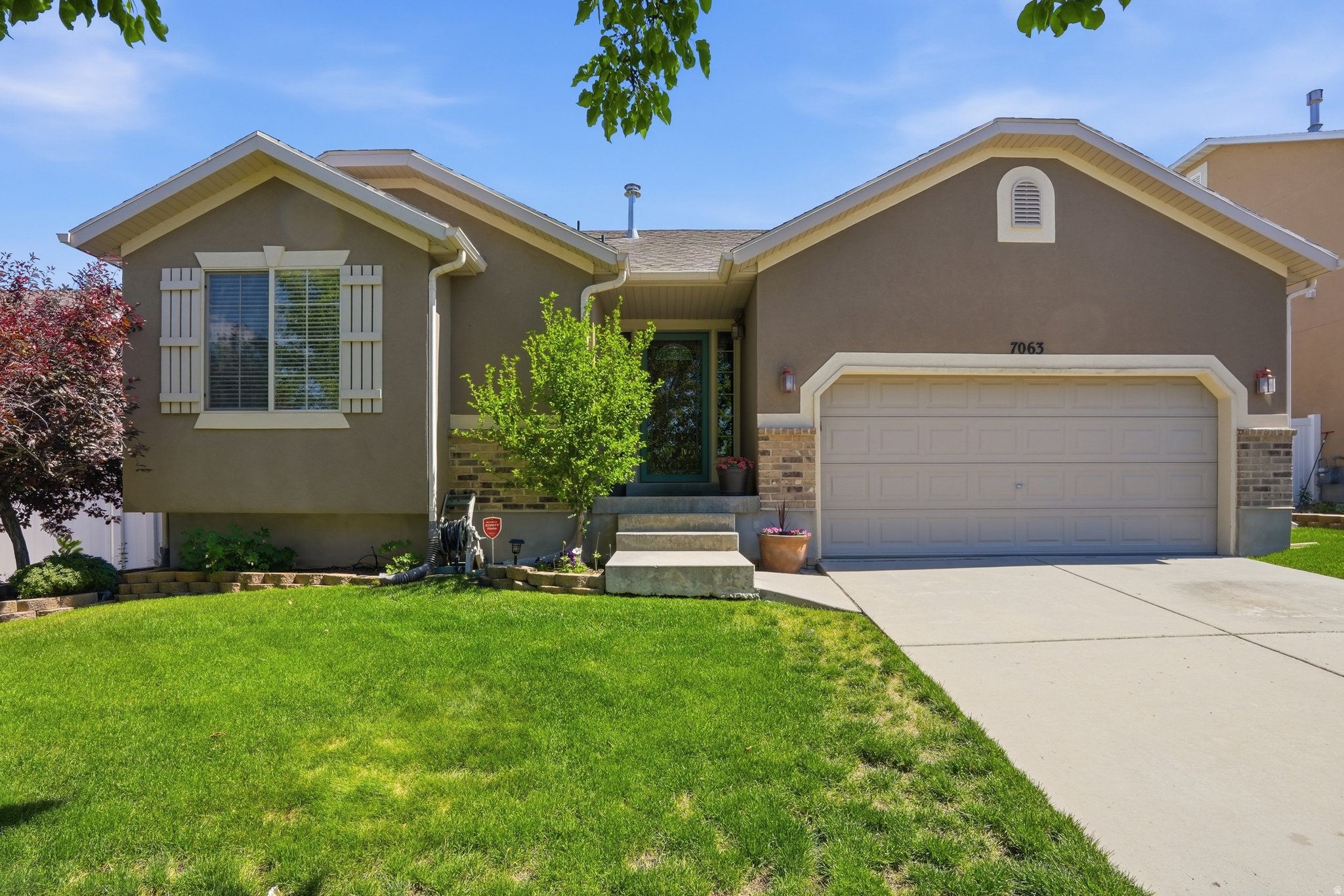 Stucco exterior featuring a two-car garage, concrete driveway, and mature landscaping