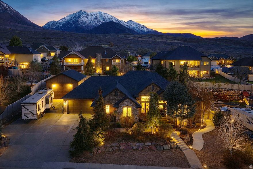 Be sure to check out the 3D and drone video tours by clicking on the tour button. This original-owner custom home is ideally situated on a quiet street in one of Santaquin's most desirable areas near the mouth of the canyon, offering stunning views and a spacious .41-acre lot with beautifully landscaped grounds, mature trees, and garden boxes. The full brick exterior is complemented by an enormous attached six-car garage with a rear pull-through door, along with a separate detached three-car garage/workshop equipped with a rail hoist and dust collection system. Inside, the home features 9-foot ceilings throughout, with select spaces opening up to impressive 14-foot ceilings. Additional highlights include plantation shutters, whole-home audio, and a thoughtfully designed layout with a formal living room or office off the foyer. The kitchen is well-appointed with double ovens, a separate gas range, granite countertops, and a tile backsplash, while the inviting living spaces include both a gas fireplace and a wood-burning stove. The spacious master suite offers a walk-in shower, separate tub, double vanities, and a walk-in closet. The fully finished walkout basement boasts 9-foot ceilings, an exercise room, and is already stubbed for a kitchenette, offering excellent potential for an accessory apartment. Additional highlights include a huge covered patio, 2x6 exterior construction with upgraded insulation, a water softener, and built-in laundry cabinetry, making this home a rare combination of quality, space, and versatility.