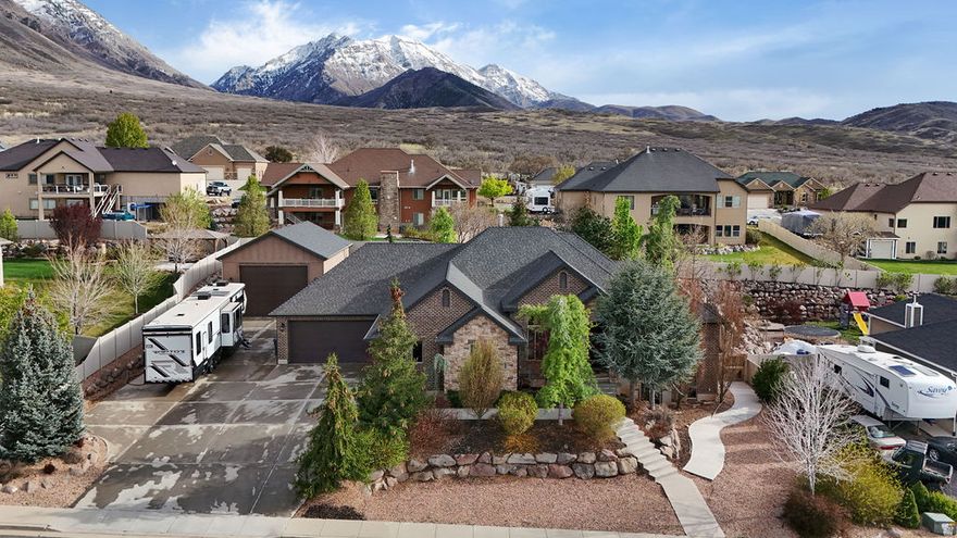 Be sure to check out the 3D and drone video tours by clicking on the tour button. This original-owner custom home is ideally situated on a quiet street in one of Santaquin's most desirable areas near the mouth of the canyon, offering stunning views and a spacious .41-acre lot with beautifully landscaped grounds, mature trees, and garden boxes. The full brick exterior is complemented by an enormous attached six-car garage with a rear pull-through door, along with a separate detached three-car garage/workshop equipped with a rail hoist and dust collection system. Inside, the home features 9-foot ceilings throughout, with select spaces opening up to impressive 14-foot ceilings. Additional highlights include plantation shutters, whole-home audio, and a thoughtfully designed layout with a formal living room or office off the foyer. The kitchen is well-appointed with double ovens, a separate gas range, granite countertops, and a tile backsplash, while the inviting living spaces include both a gas fireplace and a wood-burning stove. The spacious master suite offers a walk-in shower, separate tub, double vanities, and a walk-in closet. The fully finished walkout basement boasts 9-foot ceilings, an exercise room, and is already stubbed for a kitchenette, offering excellent potential for an accessory apartment. Additional highlights include a huge covered patio, 2x6 exterior construction with upgraded insulation, a water softener, and built-in laundry cabinetry, making this home a rare combination of quality, space, and versatility.