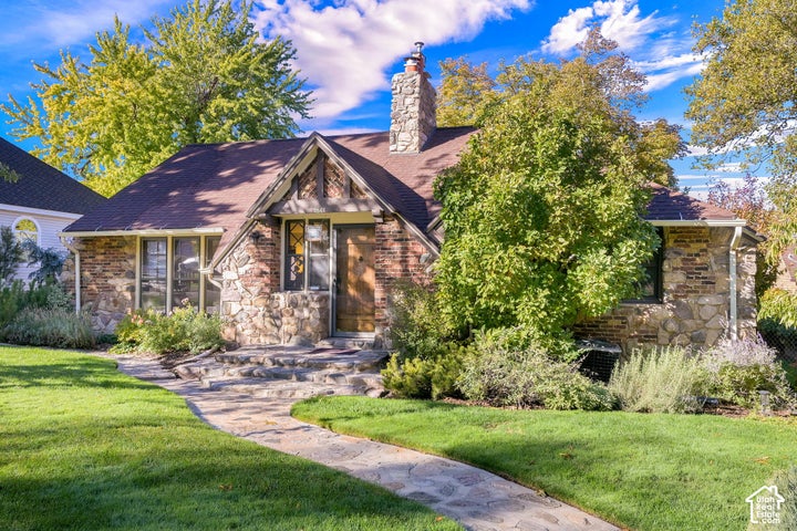 Tudor-style exterior featuring stone cladding, a prominent stone chimney, timber-accented gable, and a curved natural…