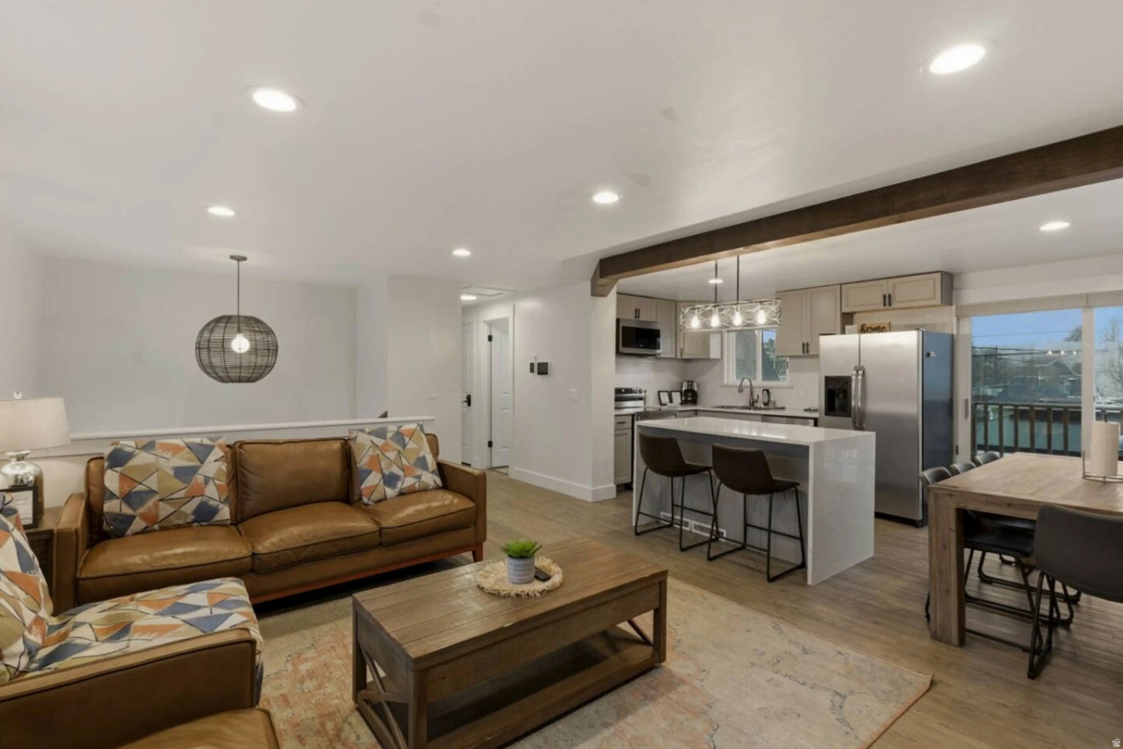 Open-concept living area with wood-finish flooring, recessed lighting, and a prominent exposed beam
