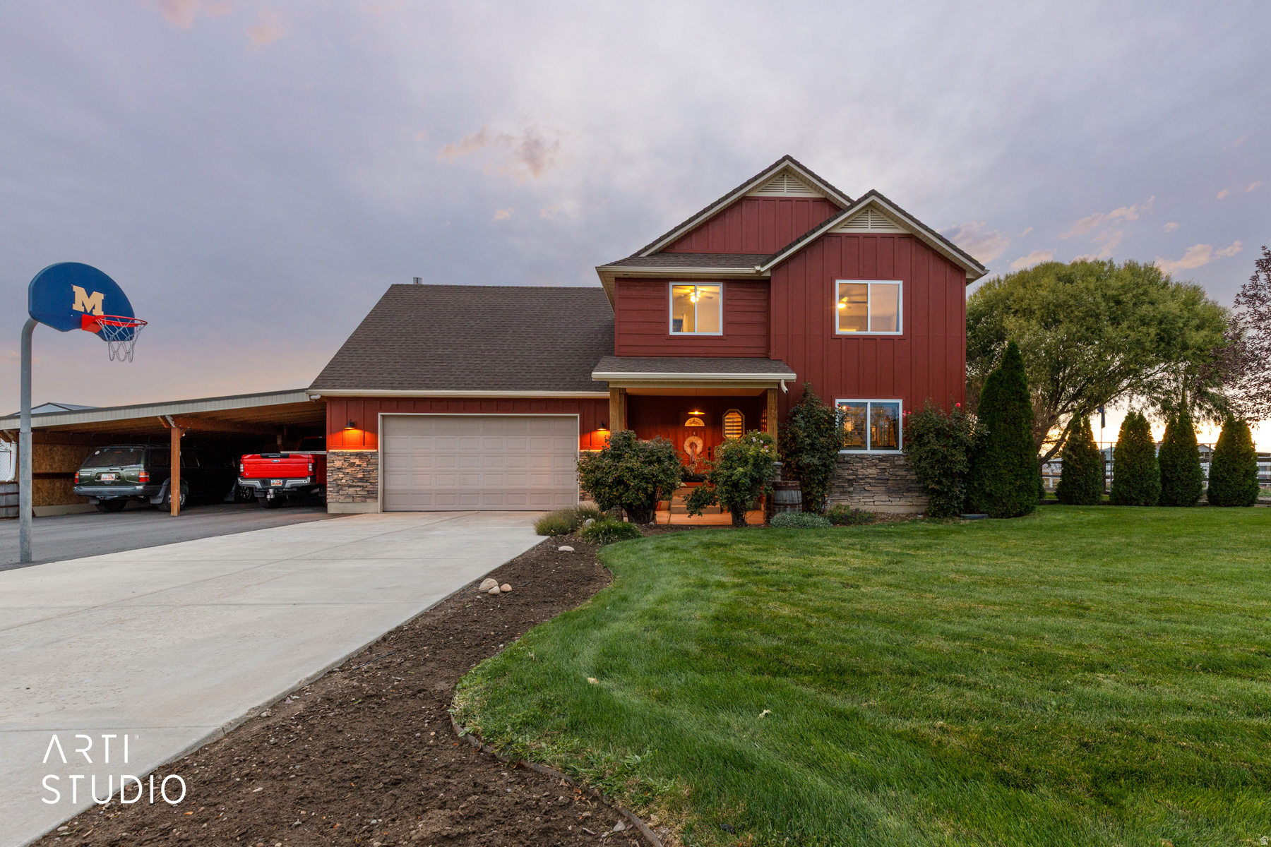 Red siding residence featuring a covered front porch, an attached garage, a multi-car carport, a concrete driveway, and a manicured lawn