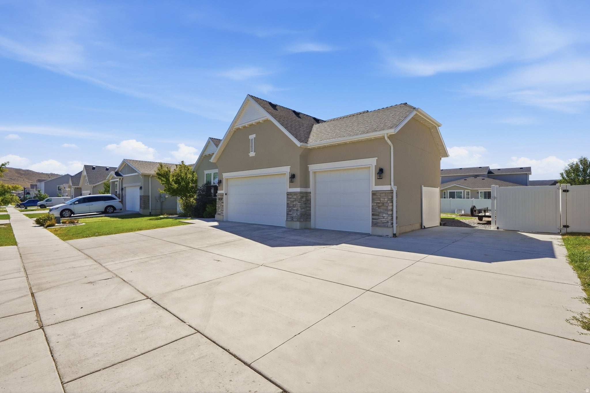 Exterior featuring stucco siding, stone accents, two-car garage, concrete driveway, and a white privacy fence