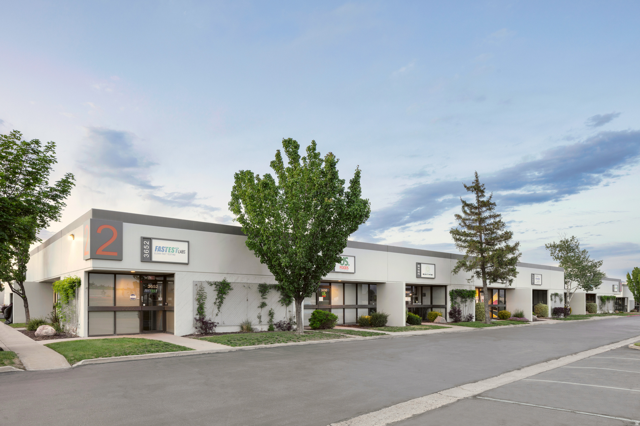 Modern commercial building with a light-colored facade, prominent signage areas, large storefront windows, dedicated entrances, and an asphalt parking lot