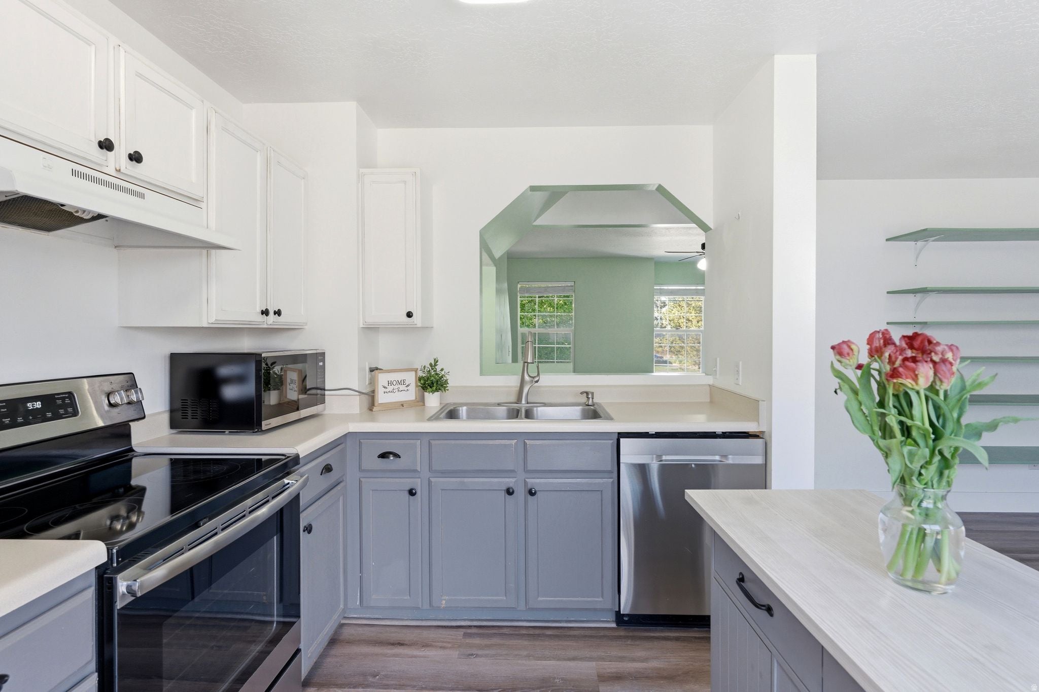 Kitchen featuring white upper cabinetry, gray lower cabinetry, stainless steel appliances, light countertops, and wood-finish flooring