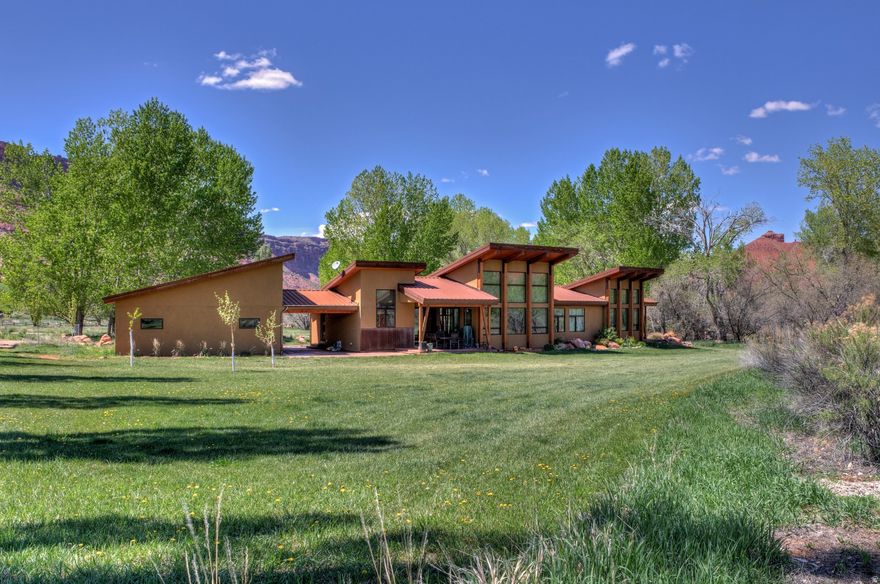 Situated on 5-acres, surrounded by breathtaking views of red rock formations and the La Sal mountains, this 4-bedroom, 3.5-bath home delivers the ultimate experience in desert living. The bright main living area features vaulted ceilings, solid hickory floors, and a wood burning fireplace, with expansive windows that frame the beauty of nature. The open plan kitchen is graced with custom built African mahogany cabinets and granite countertops. Sliding glass doors open to the porch, seamlessly blending indoor and outdoor living. Outside, a covered carport separates the home from the oversized two-car garage. The garage features a climbing wall that extends to the ceiling