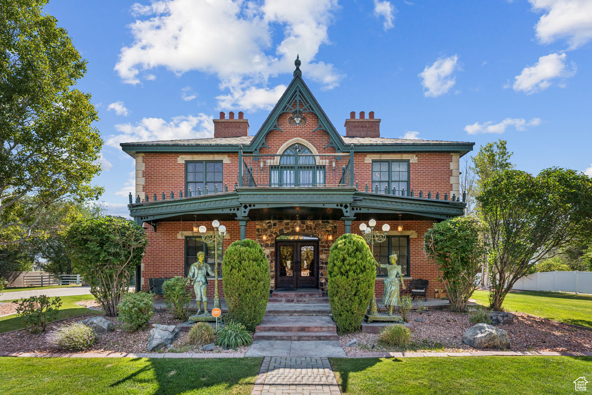 Step into timeless elegance with this exquisite Andrew Jackson Downing-inspired estate, proudly featured on the Salt Lake Parade of Homes Tour in 2004. A peaceful fountain and French sculptures lead you through a beautifully landscaped patio and into the home's grand entry. French steel doors open into a welcoming vestibule, guiding you into a spacious hall flanked by a Victorian-style parlor and a cozy lounge. The main level also features a formal dining room with French doors and a beautifully designed chef's kitchen-complete with granite countertops, Viking appliances, an ice maker, and a built-in wine cooler cellar. Thoughtfully crafted with both function and style, this home is perfect for hosting and everyday living. Upstairs, an open atrium hallway filled with natural light creates a bright, gallery-like atmosphere-ideal for showcasing collections or simply enjoying the architectural flow of the home. The second floor offers three well-appointed bedrooms, including a luxurious primary suite featuring dual walk-in closets, a cozy fireplace, two private balconies, and a custom Sego Lily stained glass window. The spa-like ensuite is adorned with a classic footed tub, elegant brass fixtures, and timeless design elements throughout. Hardwood floors on the main level and top floor have all been recently resurfaced and finished. The lower level is an entertainer's dream-ride "down south" to a western-inspired retreat featuring a billiard room, theater room, and a western saloon. A flexible office space is also located downstairs, easily used as a fourth bedroom or creative studio. The carpet in the basement and stairs to the basement has all been recently replaced with a neutral tan shade. AI photos added to show new carpet color. Outside, the property continues to impress with a carriage-style three-car garage and 1.02 acres of land-offering space for horses, gardens, or outdoor recreation. This extraordinary home blends historic charm with modern amenities, delivering a truly one-of-a-kind lifestyle.