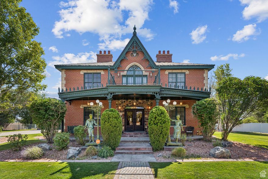 Step into timeless elegance with this exquisite Andrew Jackson Downing-inspired estate, proudly featured on the Salt Lake Parade of Homes Tour in 2004. A peaceful fountain and French sculptures lead you through a beautifully landscaped patio and into the home's grand entry. French steel doors open into a welcoming vestibule, guiding you into a spacious hall flanked by a Victorian-style parlor and a cozy lounge. The main level also features a formal dining room with French doors and a beautifully designed chef's kitchen-complete with granite countertops, Viking appliances, an ice maker, and a built-in wine cooler cellar. Thoughtfully crafted with both function and style, this home is perfect for hosting and everyday living.  Upstairs, an open atrium hallway filled with natural light creates a bright, gallery-like atmosphere-ideal for showcasing collections or simply enjoying the architectural flow of the home. The second floor offers three well-appointed bedrooms, including a luxurious primary suite featuring dual walk-in closets, a cozy fireplace, two private balconies, and a custom Sego Lily stained glass window. The spa-like ensuite is adorned with a classic footed tub, elegant brass fixtures, and timeless design elements throughout. Hardwood floors on the main level and top floor have all been recently resurfaced and finished.   The lower level is an entertainer's dream-ride "down south" to a western-inspired retreat featuring a billiard room, theater room, and a western saloon. A flexible office space is also located downstairs, easily used as a fourth bedroom or creative studio. The carpet in the basement and stairs to the basement has all been recently replaced with a neutral tan shade. AI photos added to show new carpet color.   Outside, the property continues to impress with a carriage-style three-car garage and 1.02 acres of land-offering space for horses, gardens, or outdoor recreation. This extraordinary home blends historic charm with modern amenities, delivering a truly one-of-a-kind lifestyle.