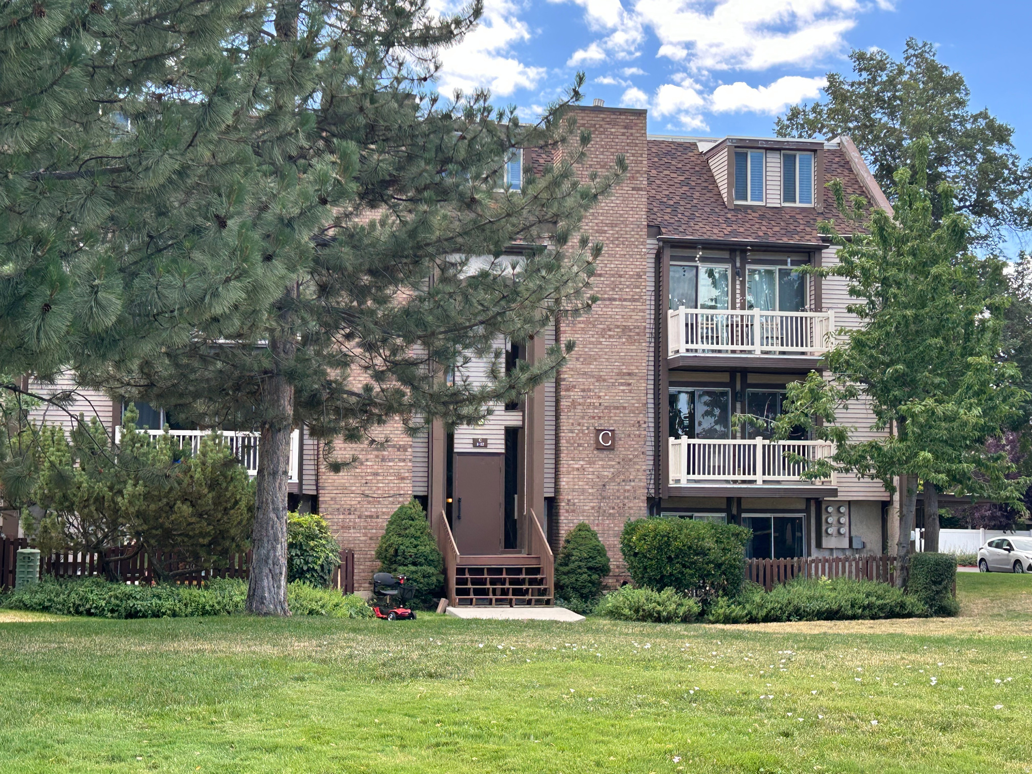 Multi-story residential building featuring brick and siding facade, private balconies with white railings, and a prominent dormer window