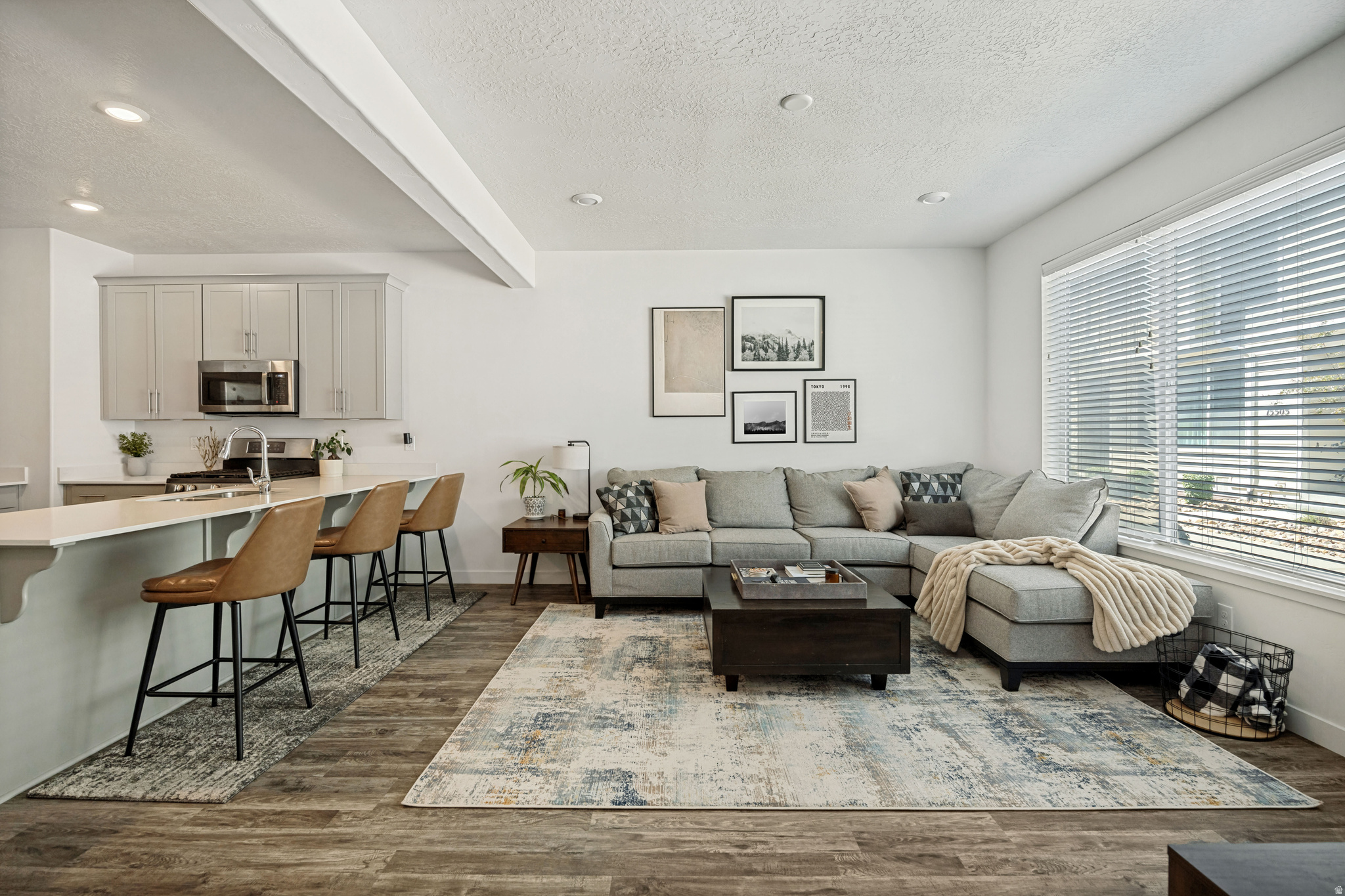 Open-concept living area featuring wood-finish flooring, recessed lighting, and a large window with blinds