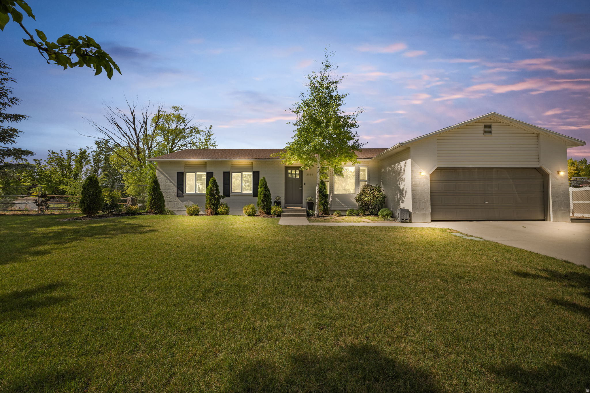 Ranch-style residence featuring a two-car garage, manicured front lawn, and mature trees