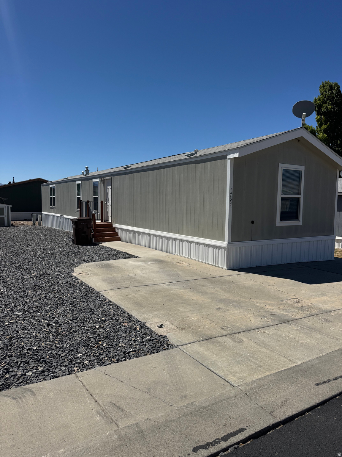Single-story residence featuring light gray siding with white trim, a gabled roofline, and a concrete driveway