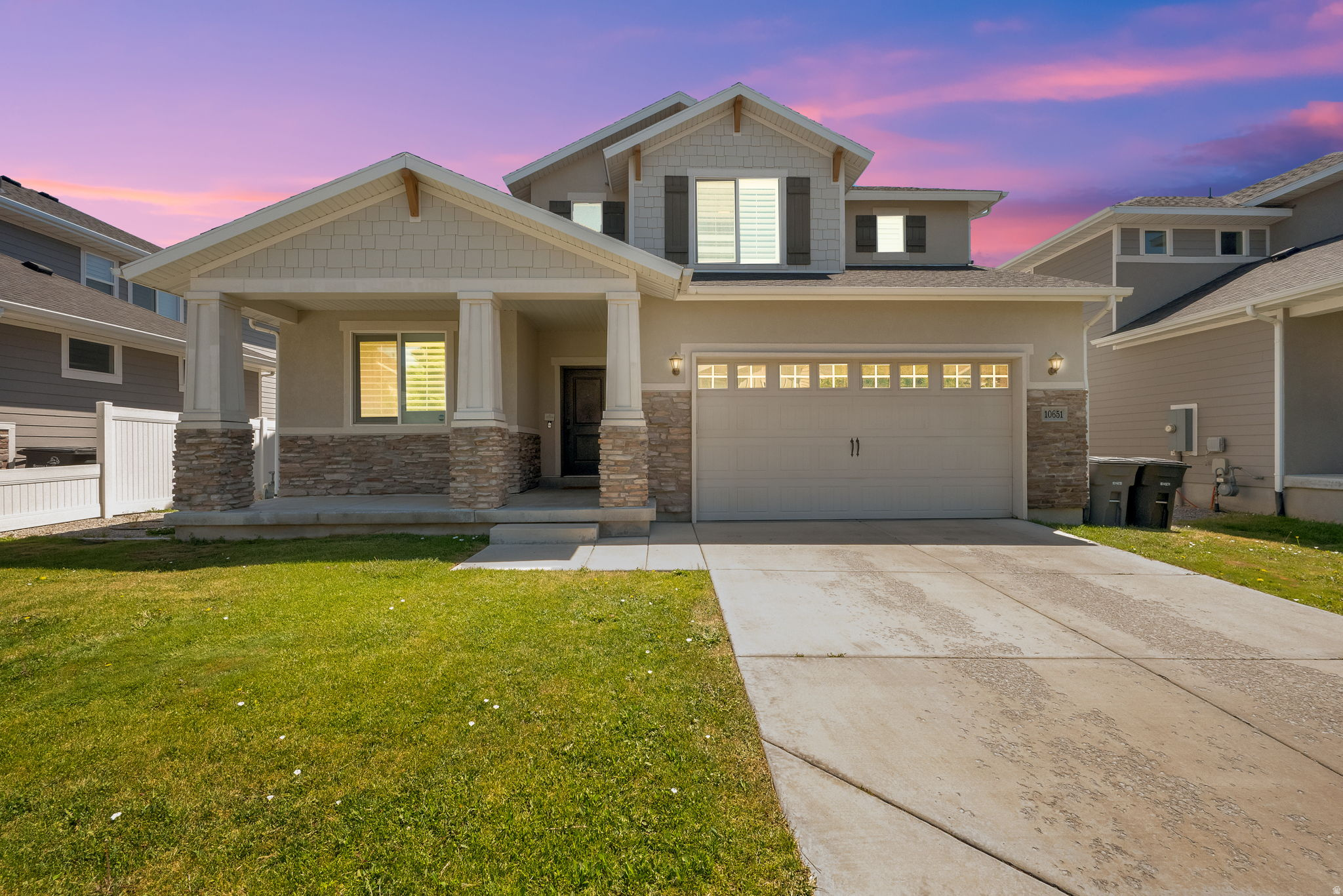 Two-story residence featuring a covered front porch with stone pillars, a two-car garage with transom windows, a concrete driveway, and an established lawn