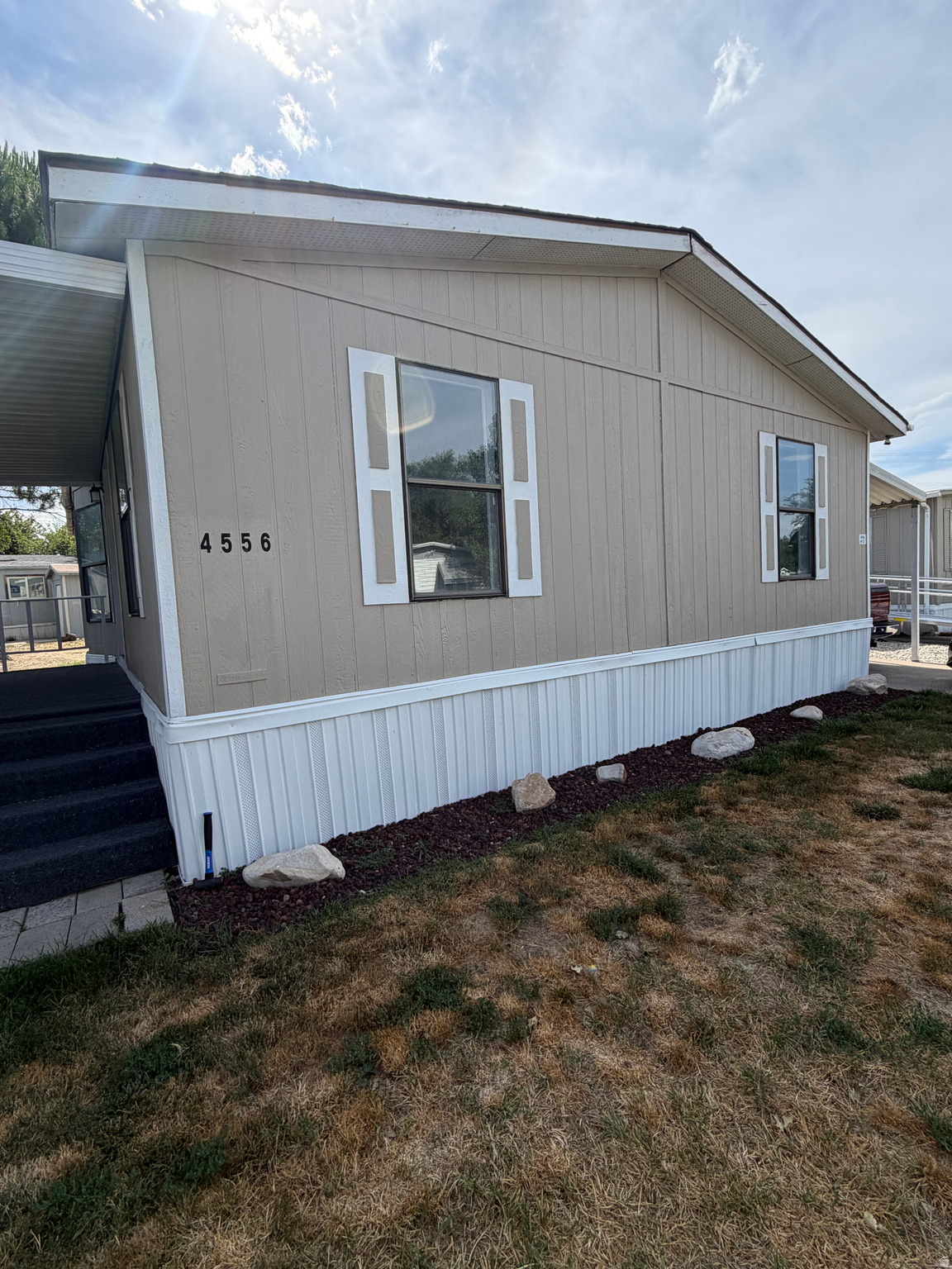 Single-story manufactured home featuring tan siding, white decorative shutters, and a covered porch entry