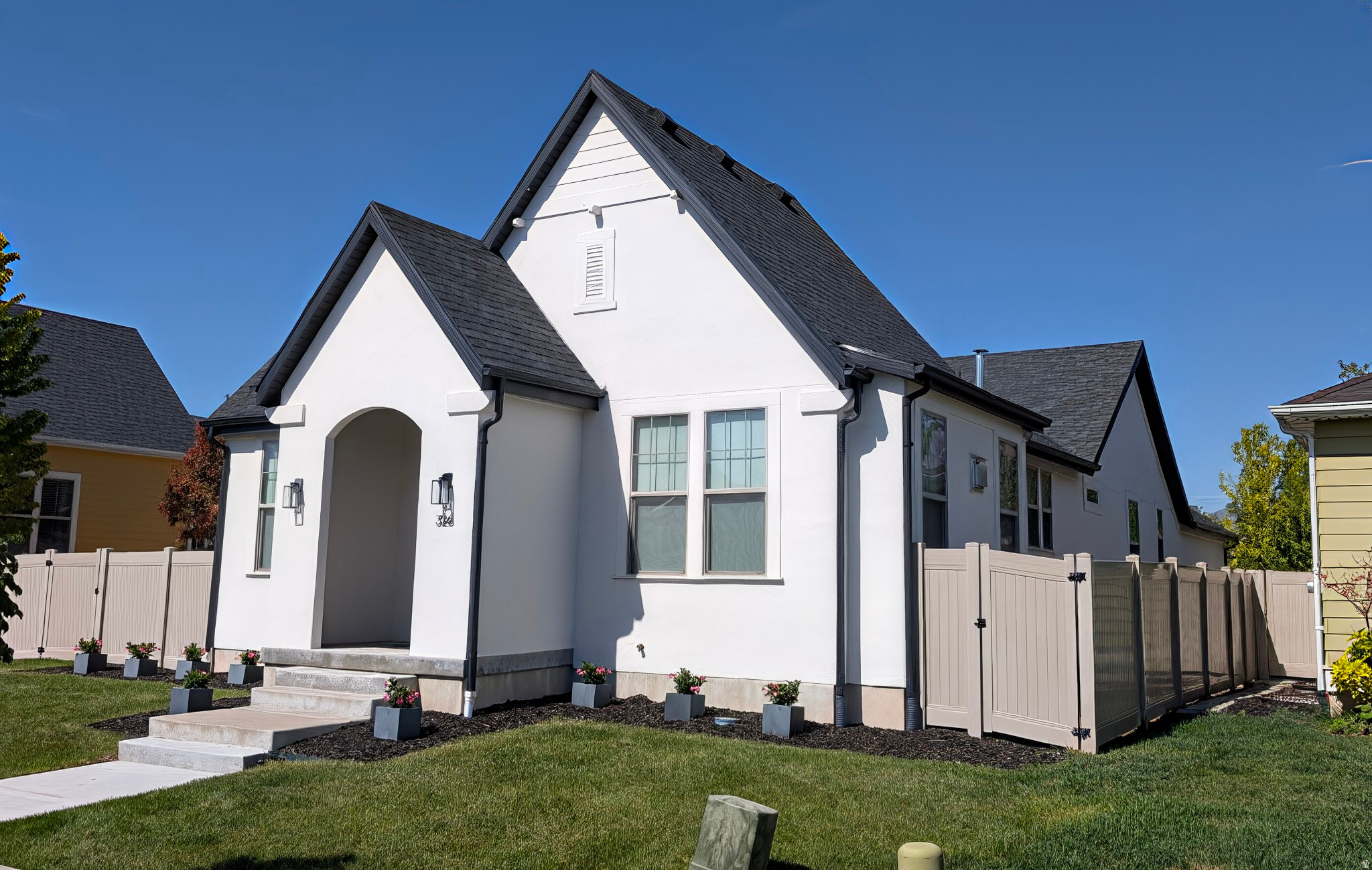 White stucco exterior with black trim, an arched entry, and a dark shingled roof