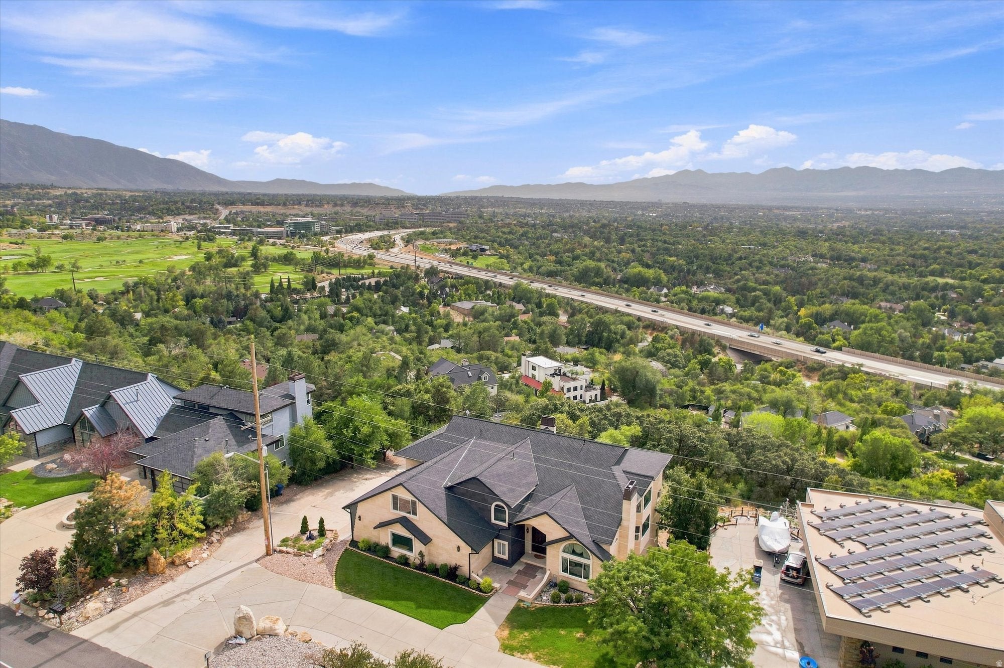 Contemporary stucco exterior with a multi-gabled dark roof, expansive paved driveway, and mature landscaping