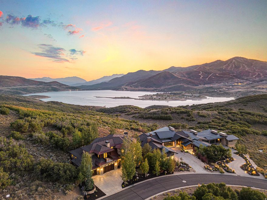 Perched above the Jordanelle Reservoir with sweeping views of Deer Valley Resort, the future Mayflower Mountain Resort, and Mt. Timpanogos, this Tuscan-inspired villa offers timeless architecture and a setting designed for gathering. Backing to open space in Hideout Canyon, the home blends European character with thoughtful functionality.  A double door entry opens to a two-story living room with imported stone flooring, Turkish light fixtures, and a striking fireplace. The chef's kitchen features Thermador appliances, including a six-burner gas stove with griddle, a double oven, and a warming drawer. A spacious island provides ample prep space, while a six-person breakfast bar and adjacent dining area with views of the mountains and reservoir make this the perfect space for group dining. A wrap-around balcony extends the living and dining spaces outdoors for entertaining, alfresco dining, or simply soaking in the scenery. Two en-suite bedrooms are also located on the main floor, along with an office, laundry room, and powder room.  The upper level offers a spacious mezzanine overlooking the living room below. The primary suite is the centerpiece of the upstairs, complete with a luxurious fireplace and panoramic views, while an additional en-suite bedroom with a private deck completes the level.  The lower level is designed for entertaining and extended stays, featuring a family room, second kitchen, theater room, bunk room with en-suite bath, a wine room, gym, and an additional half bath. Outdoor amenities include a stone patio, lawn, and fire pit, perfect for summer evenings, stargazing, or gathering around the fire after a day of skiing, boating, or mountain adventures.  This residence delivers luxury, character, and comfort in one of the area's most scenic settings. All just minutes from world-class skiing, entertainment and dining in Park City, and a short 45 minutes to Salt Lake International Airport.