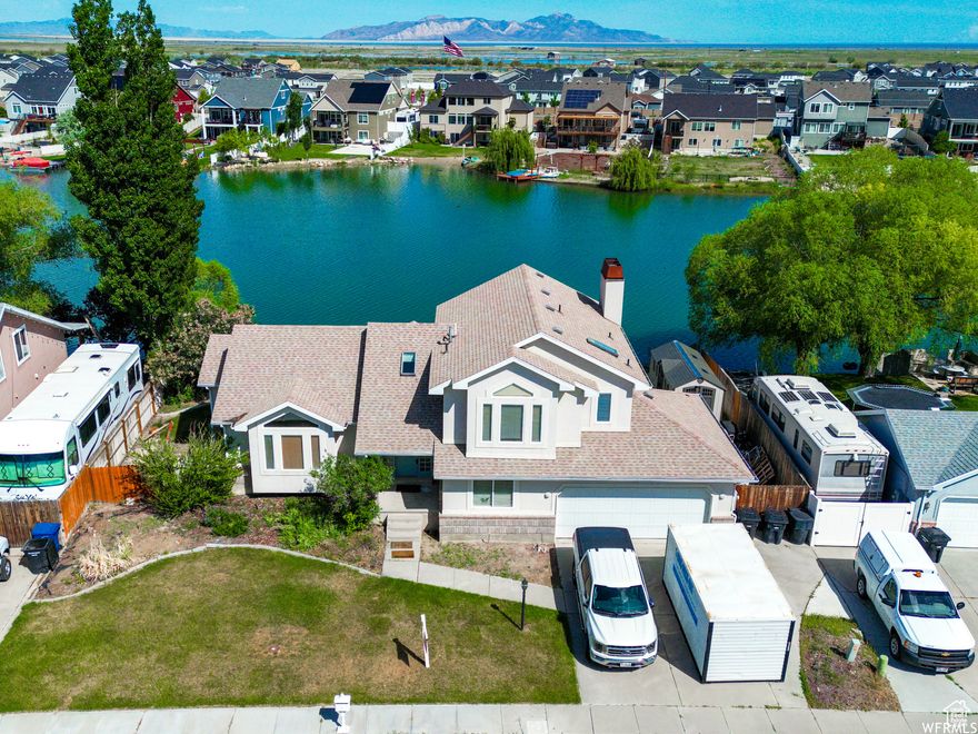 Welcome to your dream lakefront home! Perfectly situated on the water in highly desired Stansbury Park, this property offers breathtaking sunsets, panoramic lake views, and resort-style amenities right at your doorstep. Step inside to a stunning floor plan highlighted by vaulted ceilings, a grand entry foyer, and multiple skylights that flood the home with natural light. Oversized sliding glass doors frame the water views and create a seamless indoor-outdoor living experience. The master suite features its own mini-split A/C for personalized comfort, a luxurious jetted tub, and a separate shower. The fully finished basement includes a second kitchen and private entrance-ideal for extended family, guests, or rental income opportunities. Out back, relax or entertain on your spacious deck and patio with a wood-burning stove, or head down to your private dock for fishing, kayaking, and boating. This home is more than just a property-it's a lifestyle. As part of the Stansbury community, you'll also enjoy access to a pool, clubhouse, golf course, and other exclusive amenities. This is your chance to own one of the best lakefront properties in Stansbury Park. Don't miss it!