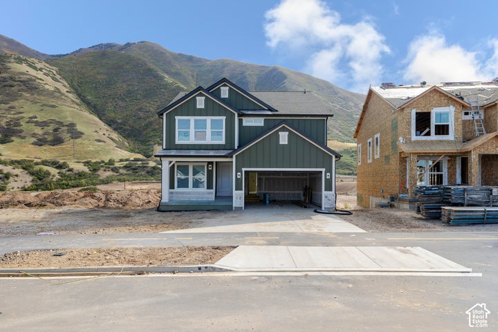 Two-story residence featuring vertical siding, stone masonry accents, a front-entry porch, an attached garage, and…