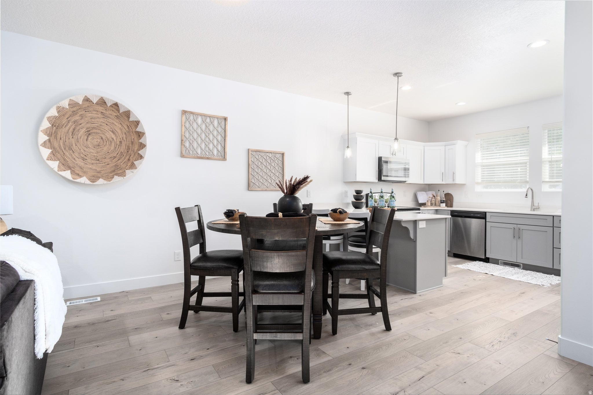Open-concept kitchen featuring white upper cabinetry, gray lower cabinetry, stainless steel appliances, and light wood-finish flooring