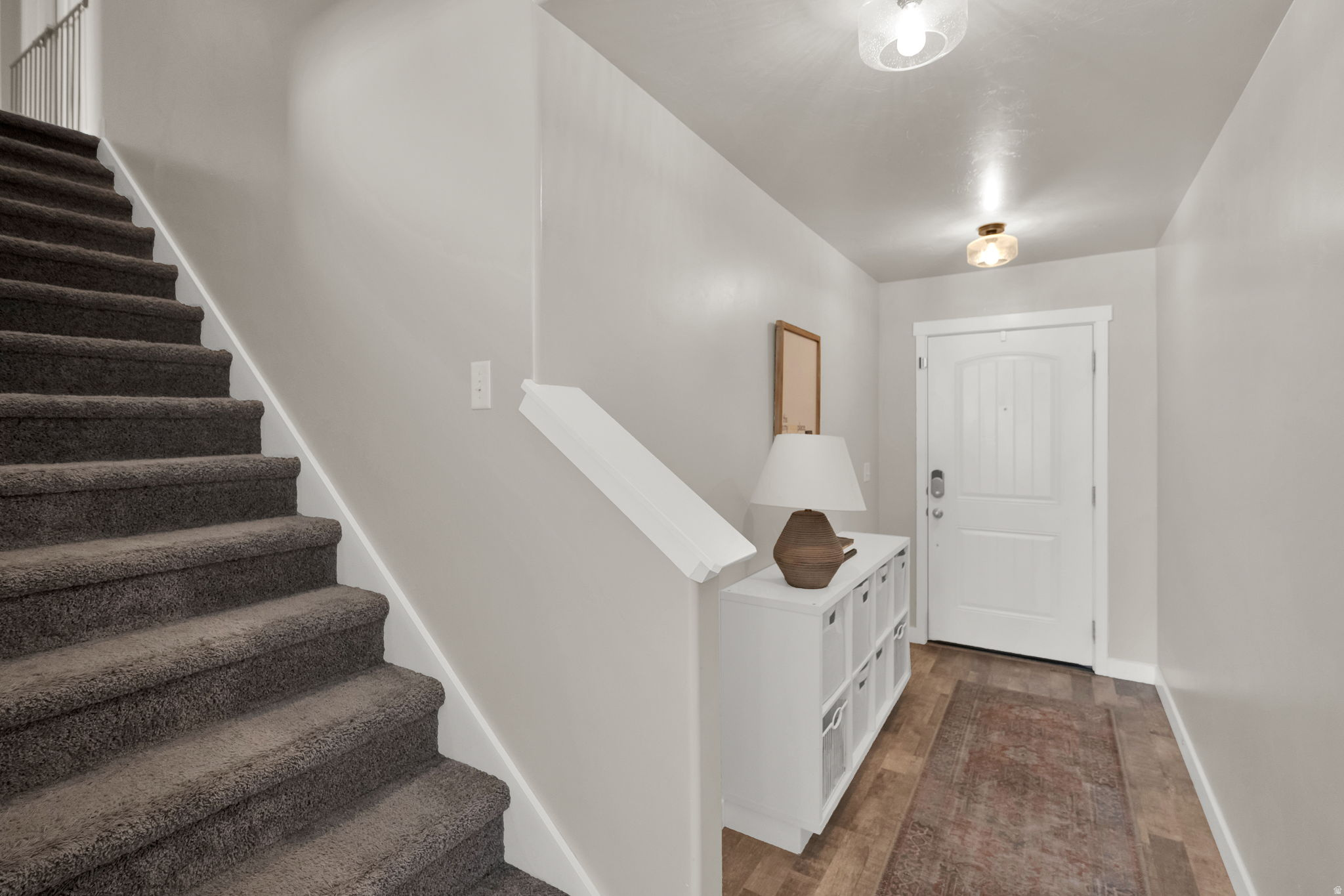 Foyer with wood-finish flooring, white paneled door with arched top light, and a carpeted staircase featuring white risers