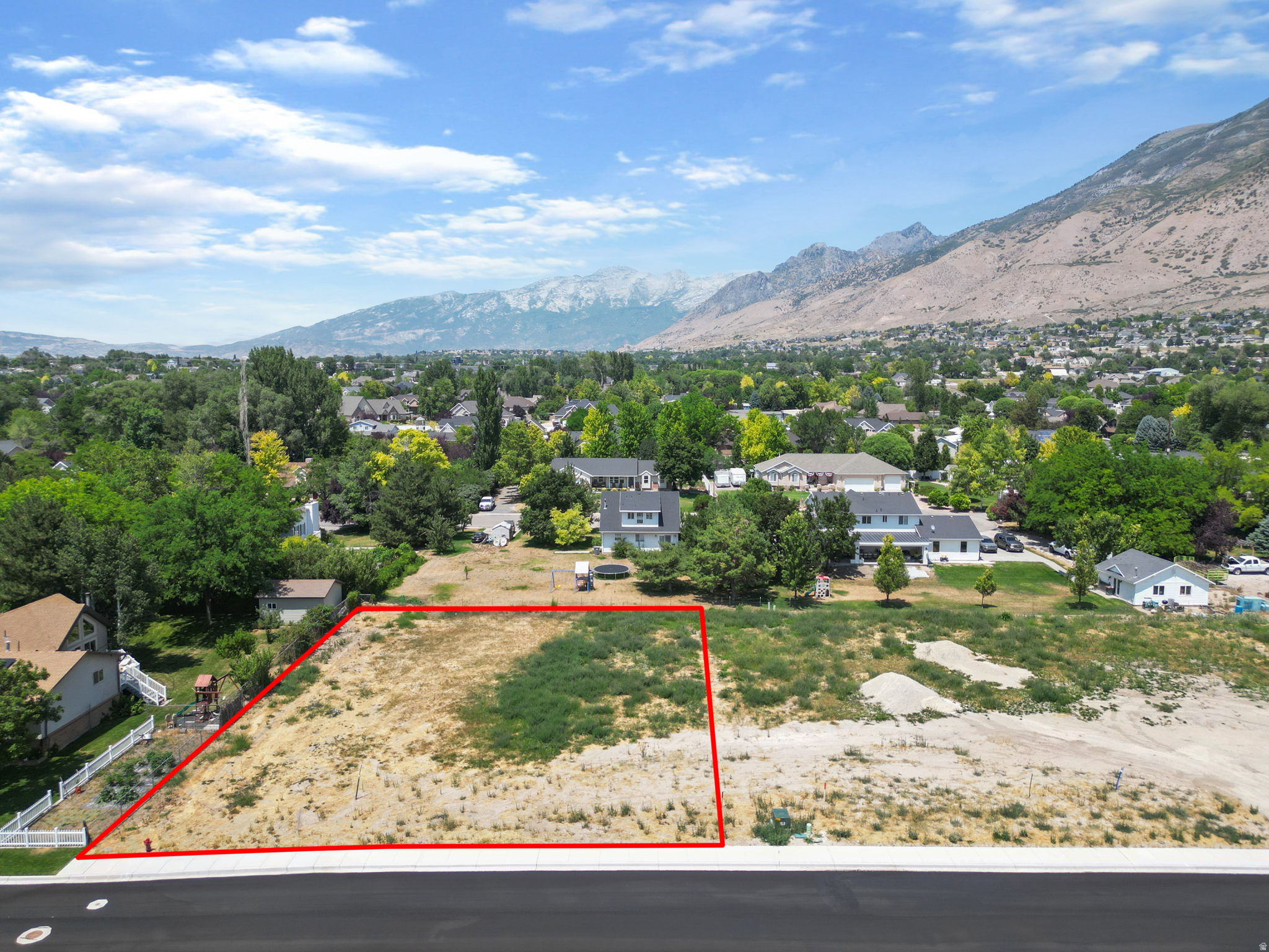 Mountain backdrop property with surrounding established homes, featuring a cleared lot, paved street frontage, and visible utilities at the property line