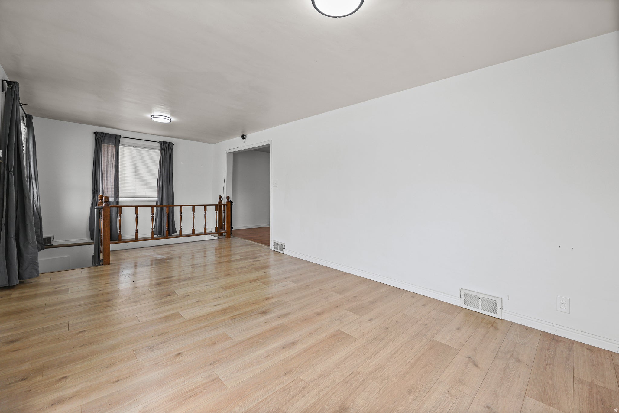 Living Room / Entry ? A bright, open living space finished with wide-plank laminate flooring, a wood-accented stair railing, and a large curtained window that fills the room with natural light.