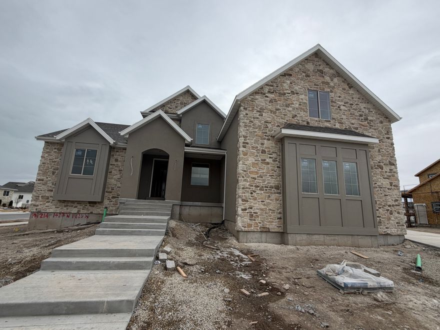 Thoughtfully designed for both style and livability, this brand new custom home in Lehi offers 5 bedrooms, 3.5 bathrooms, and refined finishes throughout. Situated on a generous 1/3 acre lot, the home provides space, natural light, and intentional design in a sought after neighborhood with no HOA. At the heart of the home is a beautifully appointed kitchen featuring tailored cabinetry, a statement range hood, a walk through pantry with dual entry, a Forno 8 burner gas range, and full size refrigerator and freezer. Two story living room ceilings and expansive windows fill the home with natural light. Step outside to the covered deck overlooking the spacious backyard, creating an ideal setting for both everyday living and entertaining. The main level primary suite offers an upscale private retreat with a freestanding soaking tub, oversized shower, and walk in closet. Upstairs includes four additional bedrooms, a playroom, two full bathrooms, and a second full laundry room, with a convenient Jack and Jill layout between two bedrooms. The walkout basement is designed for easy future completion and can be finished as an ADU. A three car garage provides ample parking and storage. Ideally located near shopping, dining, schools, and the Silicon Slopes corridor. Estimated completion: late March / early April 2026.