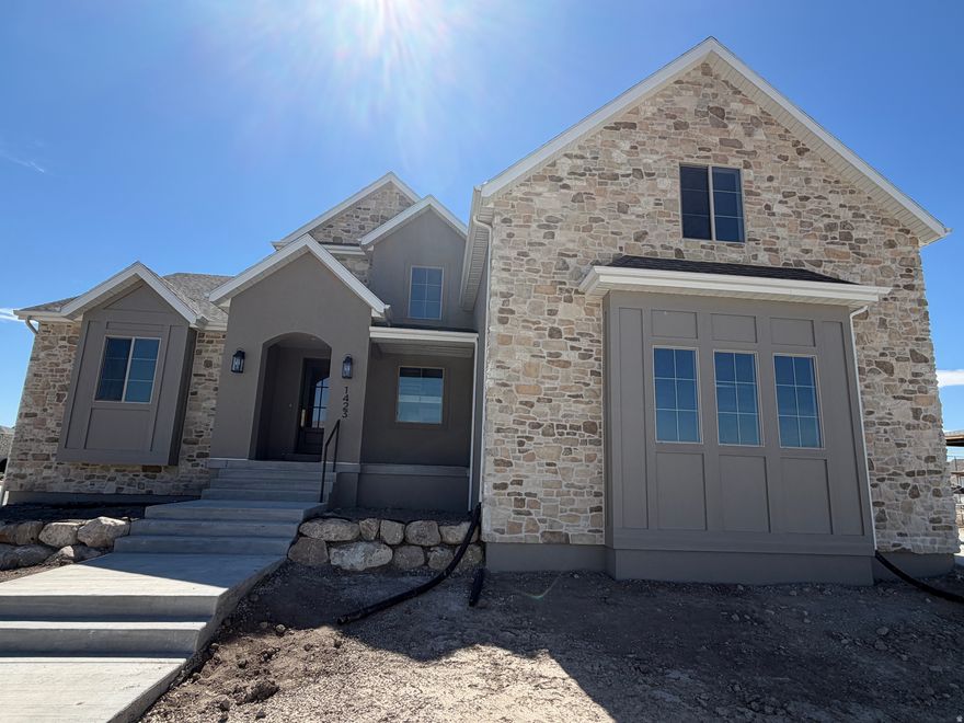 Thoughtfully designed for both style and livability, this brand new custom home in Lehi offers 5 bedrooms, 3.5 bathrooms, and refined finishes throughout. Situated on a generous 1/3 acre lot, the home provides space, natural light, and intentional design in a sought after neighborhood with no HOA. At the heart of the home is a beautifully appointed kitchen featuring tailored cabinetry, a statement range hood, a walk through pantry with dual entry, a Forno 8 burner gas range, and full size refrigerator and freezer. Two story living room ceilings and expansive windows fill the home with natural light. Step outside to the covered deck overlooking the spacious backyard, creating an ideal setting for both everyday living and entertaining. The main level primary suite offers an upscale private retreat with a freestanding soaking tub, oversized shower, and walk in closet. Upstairs includes four additional bedrooms, a playroom, two full bathrooms, and a second full laundry room, with a convenient Jack and Jill layout between two bedrooms. The walkout basement is designed for easy future completion and can be finished as an ADU. A three car garage provides ample parking and storage. Ideally located near shopping, dining, schools, and the Silicon Slopes corridor. Estimated completion: late March / early April 2026.