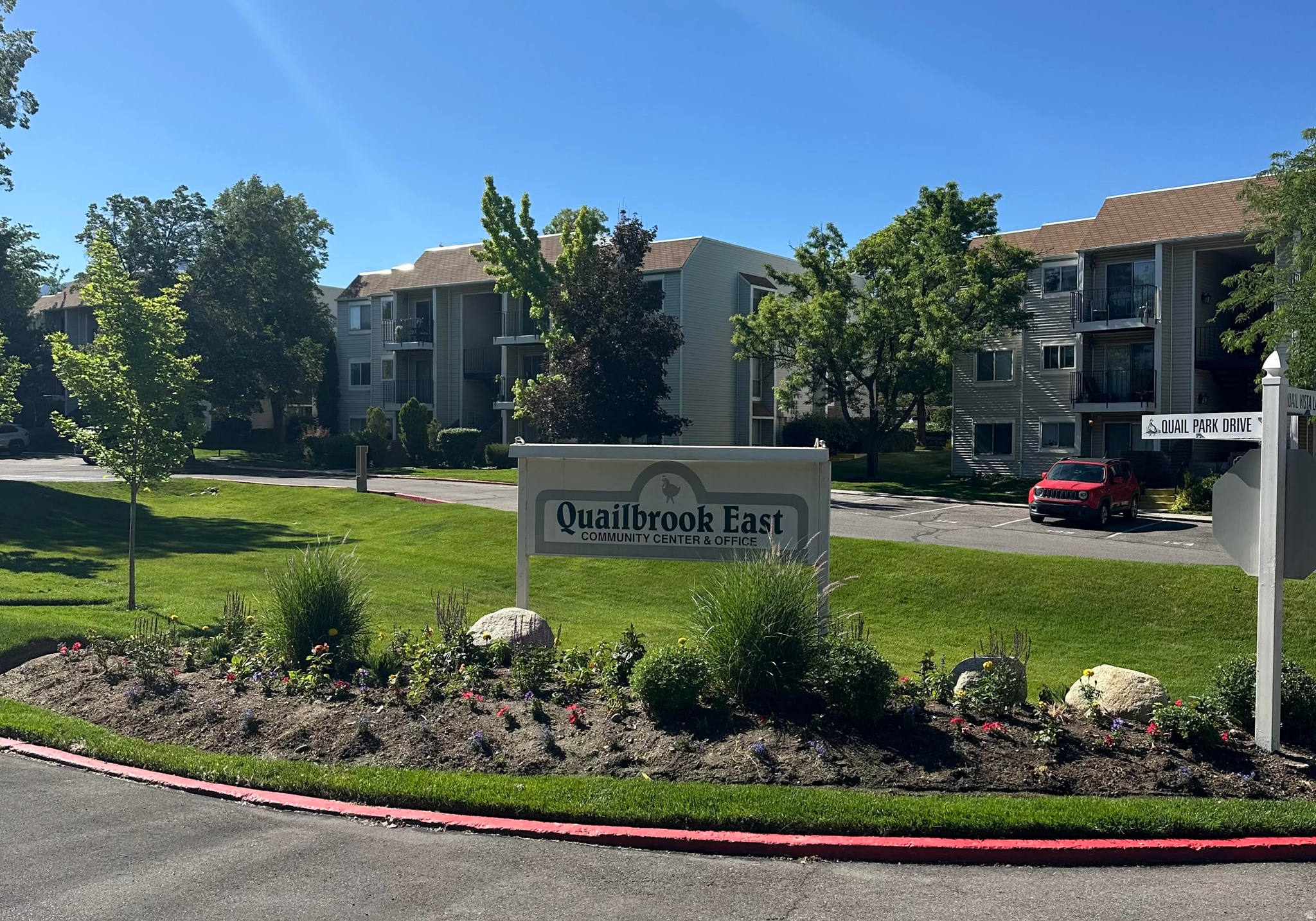 Landscaped entry featuring a community sign, mature trees, and manicured lawns