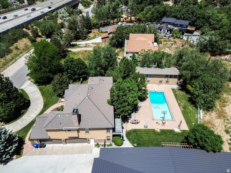 Aerial view showcasing a residential compound with a sparkling resort-style swimming pool, expansive manicured grounds with mature tree coverage, multi-structure layout with neutral-toned roofing, and proximity to major thoroughfare access