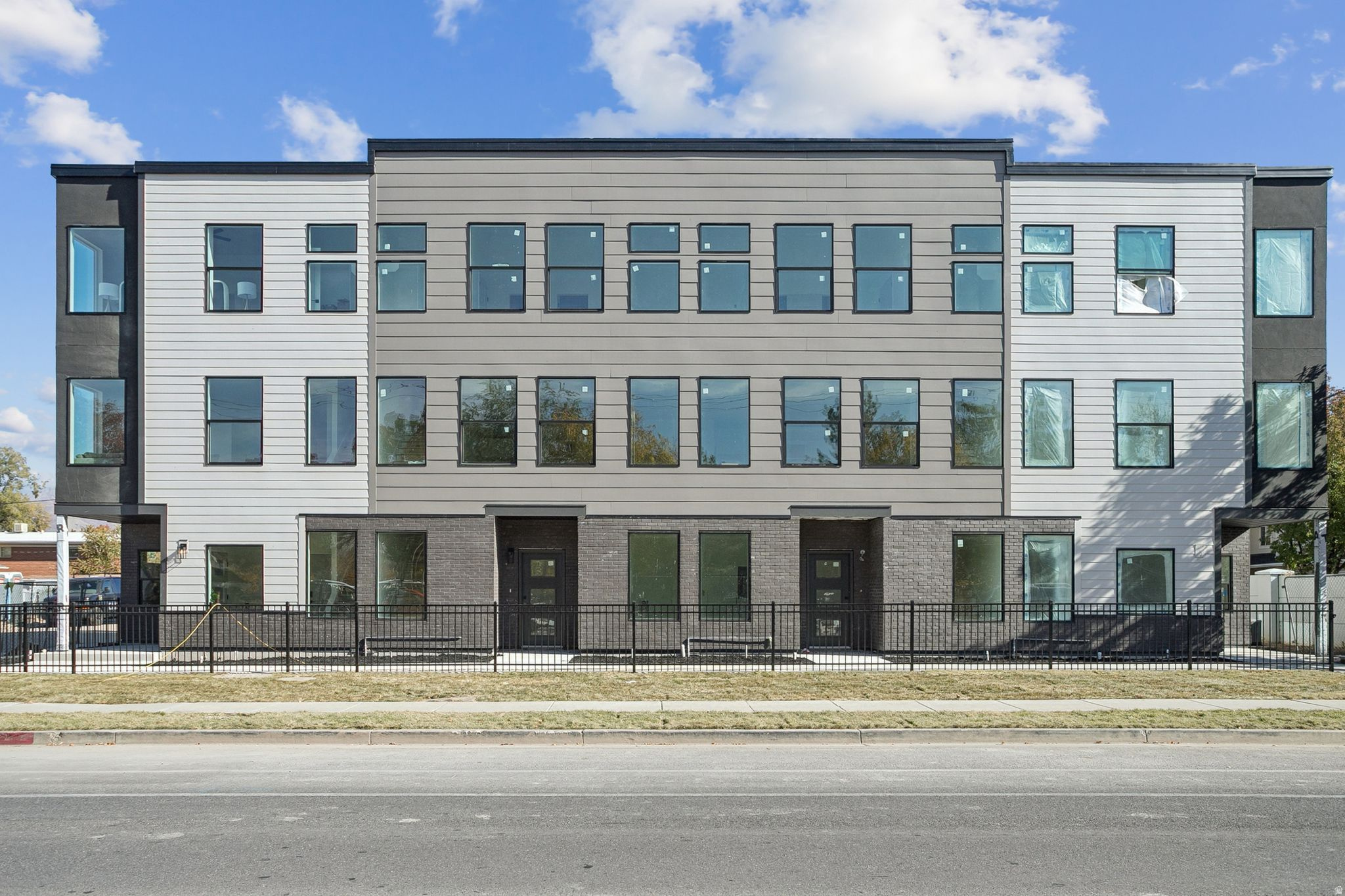 Contemporary multi-level facade featuring varied siding panels in light and dark gray, black brick accents, and numerous large windows