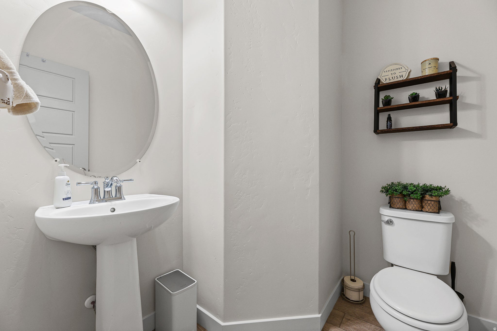 Powder room featuring a pedestal sink with chrome faucet, large circular mirror, and neutral tile flooring