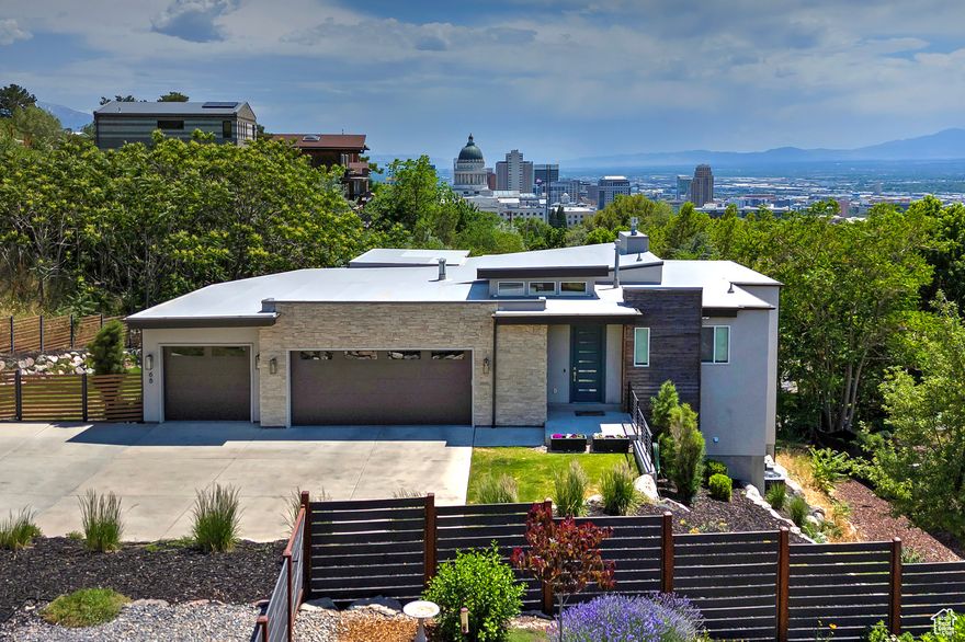 Perfectly positioned above the Capitol in the exclusive Columbus Court gated community, this spectacular contemporary home offers unmatched privacy and panoramic views of downtown Salt Lake City, the valley, and surrounding mountains. The striking exterior showcases clean architectural lines, tiered roofing, stacked stone, warm wood accents, and sleek flat-panel garage doors.  Step inside to a sunlit entry with soaring ceilings, a dramatic sputnik chandelier, and expansive windows that flood the space with natural light. High-end finishes are featured throughout, including hardwood floors, custom steel railings, vaulted ceilings, recessed lighting, window shades, and a stacked stone gas fireplace.  The gourmet kitchen is designed to impress with quartz countertops, custom cabinetry, a center island, tile backsplash, stainless steel appliances, a gas range, chef's hood, and stylish pendant lighting. The open-concept great room flows effortlessly onto a large covered composite deck with iron railings-ideal for entertaining or simply soaking in the cityscape and mountain views.  Retreat to the grand primary suite with a private balcony, stunning views, an organized walk-in closet, and a spa-like bath complete with a euro-glass shower, soaking tub, dual vanity with quartz counters, and chrome fixtures.  The finished walkout lower level includes a bedroom, two full bathrooms, a spacious recreation room, and direct access to the backyard oasis-featuring a hot tub, cold plunge, and cedar sauna. Enjoy serene mornings and city lights by night from your private sanctuary.  Set on a beautifully landscaped .69-acre lot with lush lawn, native vegetation, rock accents, waterwise plants, and a full sprinkler system-this home offers the rare combination of modern luxury, unmatched privacy, and breathtaking views in one of Salt Lake's most coveted neighborhoods.