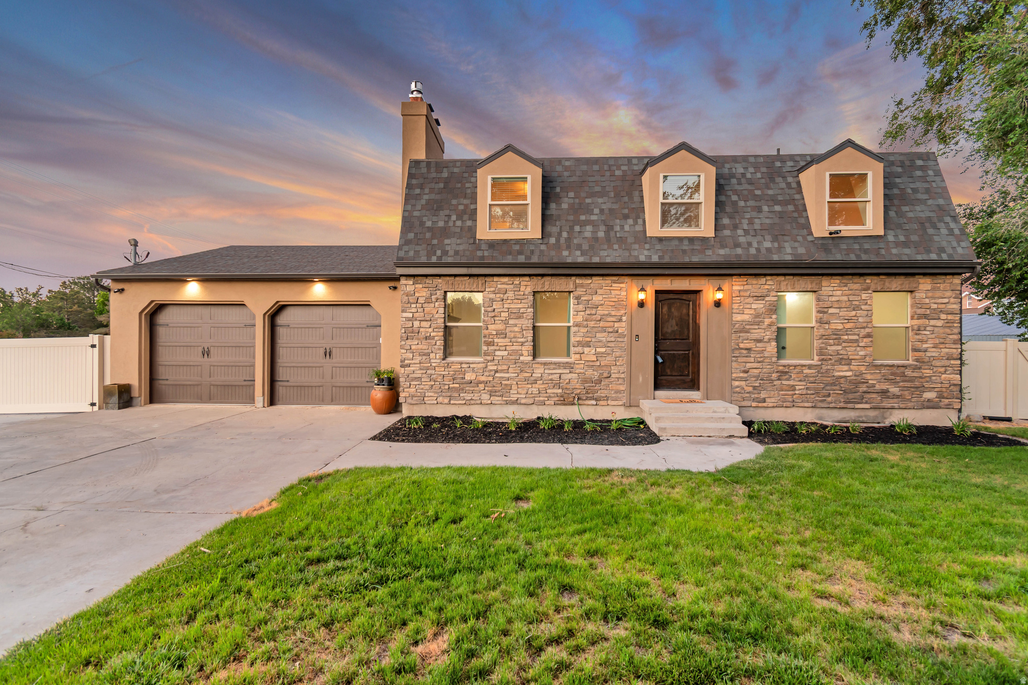 Two-story residence featuring a stone and stucco exterior, a dark shingle roof, and three dormer windows