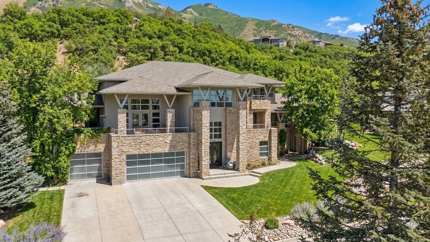 Where modern architecture meets a protected mountain backdrop, The Skyline Modern is a striking architectural residence where refined design, advanced engineering, and everyday livability converge. This exceptional home showcases uncompromising craftsmanship and globally sourced materials, beginning with the dramatic stainless-steel staircase featuring imported glass steps from Singapore-a true statement piece that sets the tone for the entire home. The main living space is expansive and inviting, defined by vaulted ceilings and a two-way fireplace that seamlessly connects indoor living with an outdoor balcony-ideal for entertaining, quiet evenings, or enjoying the surrounding natural beauty. Floor-to-ceiling mirrored UV-protected windows provide privacy while preserving natural light and views throughout. At the heart of the residence is a gourmet chef's kitchen, appointed with KitchenAid Pro Series appliances, custom bamboo cabinetry, quartz countertops, and a dedicated wine refrigerator-perfectly designed for both daily living and elevated entertaining. The main-level bedroom retreat offers exceptional comfort, featuring two private decks and a spa-inspired bath with an oversized shower. Upstairs, the primary suite is a true sanctuary, complete with heated floors, a stand-alone soaking tub, a multi-head shower, and a private balcony designed for peaceful mornings and quiet evenings. Additional upstairs bedrooms share a Jack-and-Jill bathroom, while a dedicated laundry room with abundant storage enhances everyday functionality. The lower level adds remarkable versatility with a private bedroom or mudroom featuring a separate entrance, ideal for guests or multigenerational living. Also located on this level is a fully built in-home salon, complete with a professional hair sink and its own dedicated client entrance-perfect for a private studio, live-work arrangement, or creative space, all while maintaining separation from the main living areas. Outdoor living is intentionally secluded and exceptionally rare. The backyard enjoys no rear neighbors and directly borders the mountain, creating a setting of true privacy and permanence-where the landscape becomes a natural extension of the property. Multiple outdoor decks overlook this protected backdrop and are equipped with a premium sound system, offering an unparalleled environment for entertaining or unwinding in complete seclusion. This residence is as intelligent as it is beautiful, featuring C-5 cabling, an automatic backup power generator, radiant heat plumbing on the lower level, three Lennox A/C systems, and a heated garage with extra storage, ensuring year-round comfort and reliability. One of the home's most distinctive amenities is the indoor swimming pool, designed for effortless enjoyment with an automated chlorine and salt system and a dedicated dehumidification system that maintains a warm, comfortable environment in every season. The Skyline Modern is a rare offering-architectural, intentional, and meticulously designed-delivering a seamless blend of luxury, privacy, technology, and lifestyle flexibility.