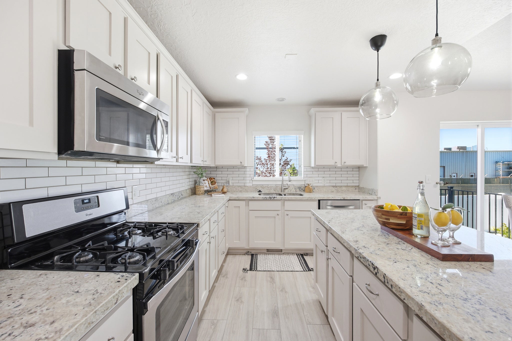 Kitchen featuring light-toned cabinetry, light granite countertops, stainless steel appliances, and a white subway tile backsplash