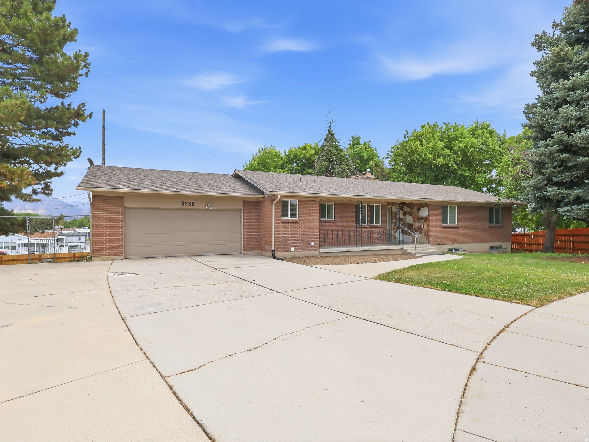 Brick exterior with a stone accent wall, featuring a two-car garage, mature landscaping, and an expansive concrete driveway