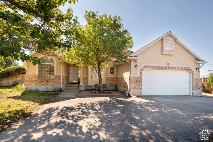 Single-story exterior featuring a stucco and brick facade, an attached two-car garage, an arched window, and concrete…