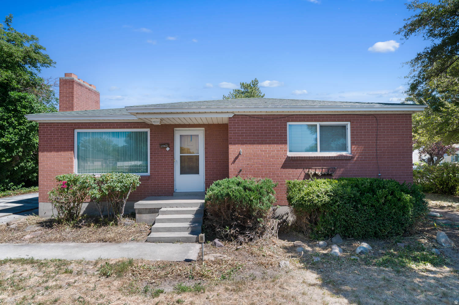 Brick exterior residence featuring a front porch with concrete steps, a white entry door, and multiple windows