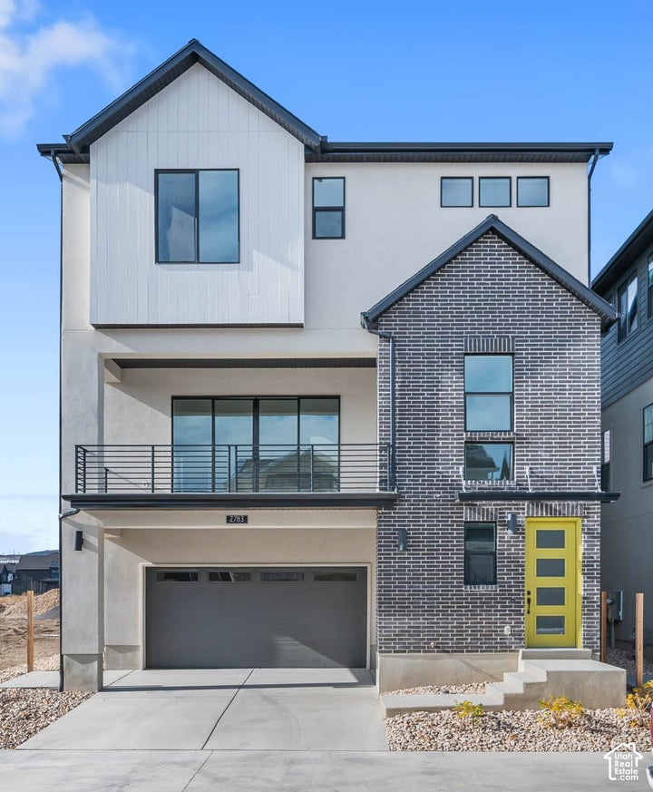 Contemporary exterior featuring mixed material cladding, an attached two-car garage, a second-story balcony with metal…