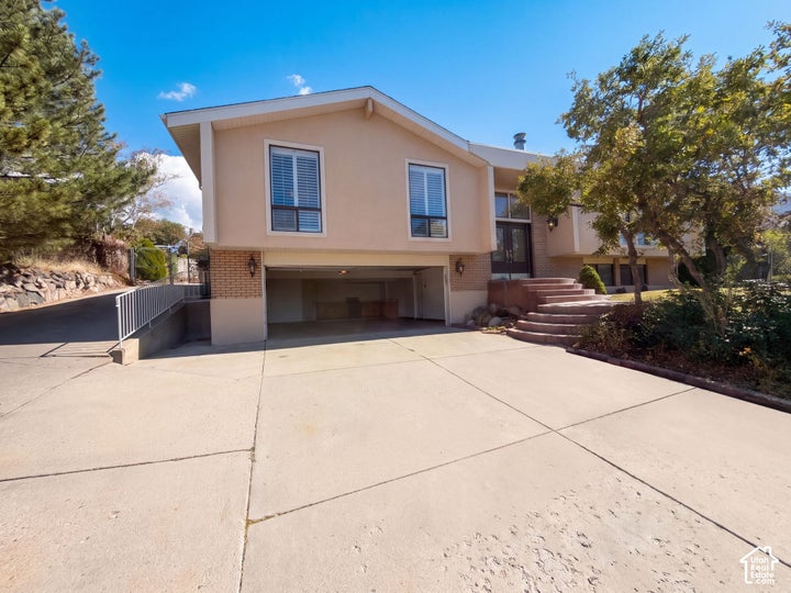 Multi-level exterior featuring a smooth stucco facade, brick lower-level accent, integrated two-car garage, and concrete…