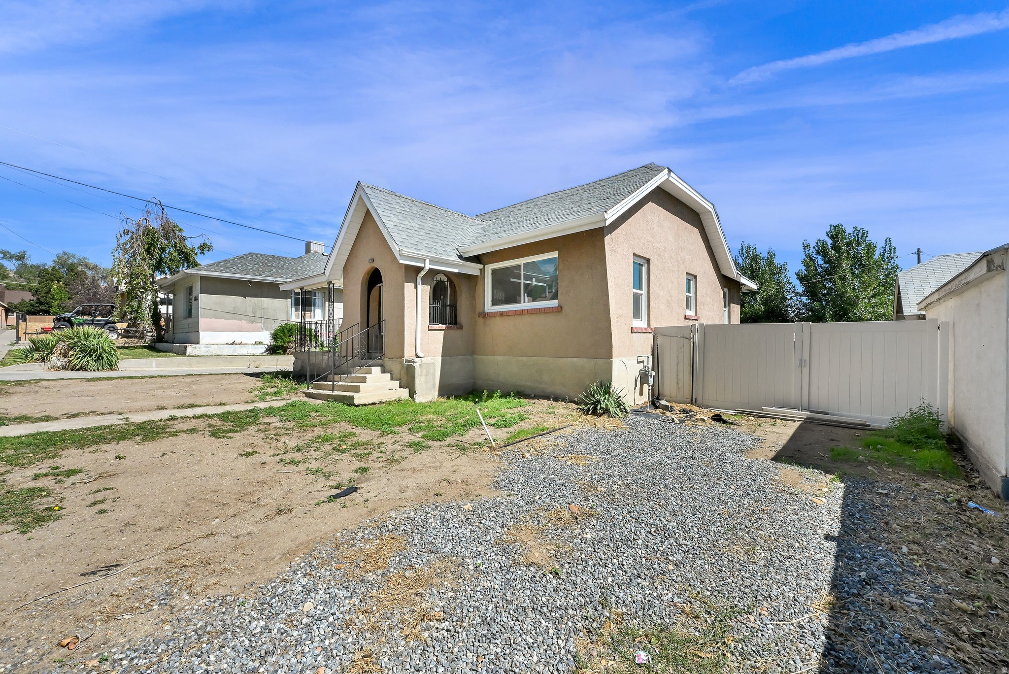 Stucco exterior with a pitched roof, front entry with steps and handrails, and a gravel driveway