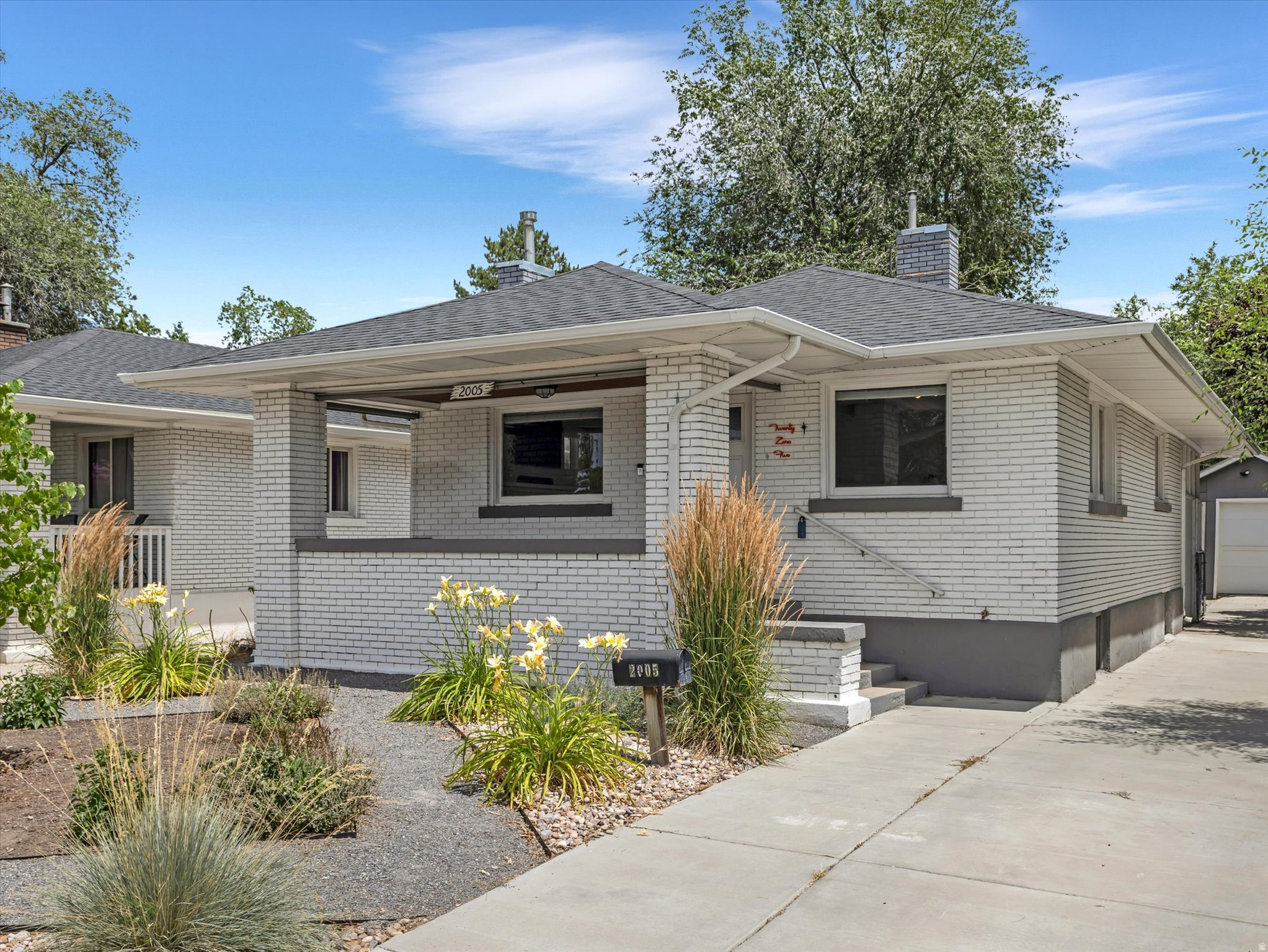 Single-story residence featuring light-colored brick exterior, dark grey trim, and a dark shingle roof