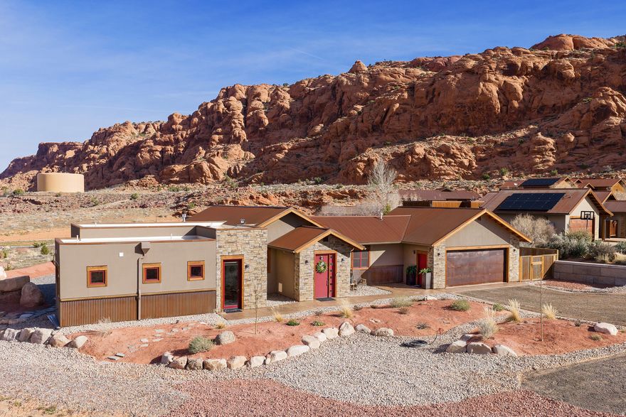DESERT LIVING AT ITS BEST in this stunning luxury home nestled among beautiful towering red rocks in MOAB, Utah. This home features elegant rustic charm with soaring Alder ceilings, a rugged floor-to-ceiling stone fireplace, knotty Alder cabinetry, and leathered quartzite countertops. The chef's kitchen offers abundant prep space, apron sink with oil-rubbed bronze faucet, double ovens (electric convection + six-burner gas range), side-by-side stainless refrigerator, massive island with pull-outs, Butler's pantry, wet bar with wine fridge and ice maker, and a built-in office area.  The light-filled living room opens seamlessly to both a private courtyard and expansive patio, creating ideal indoor-outdoor flow. The primary suite is a true retreat with automatic blinds, patio access, and a spa-inspired bath featuring a luxury walk-in shower with rain head, body sprays, and handheld sprayer-- plus plumbing for a sauna or soaking tub, with High-honed travertine countertops and vessel sinks to complete the spa feel. Three additional bedrooms feature en-suite bathrooms with stone countertops and walk-in closets and built-in shelving. The fourth bedroom includes a loft bed with additional seating or office space below. Just off the kitchen is a guest bath with walk-in tile shower, stone flooring, and honed marble countertop with chiseled edge. The laundry room and garage are conveniently adjacent, offering butcher block folding counters, a large workbench, and extra cabinet storage.  Enjoy multiple outdoor living spaces, including a private courtyard with massive stone walls, built-in hot tub, fire feature, surround sound, and bar seating. The extended stone patio includes a built-in gas firepit, massive red rocks, flagstone pathways, and is plumbed for an outdoor kitchen and BBQ. You will love the high tech features in this home including; smart thermostat, built in alarm system, front door google camera, speakers and TV that all work from your phone. All information deemed to be reliable by the listing office; buyer to verify all.