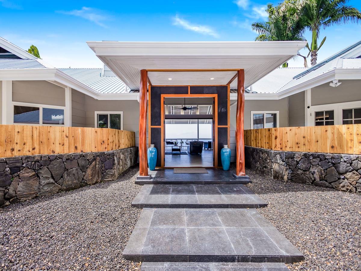 Modern home entrance with timber portico, lava-rock walls, and ocean visible through the open doorway.