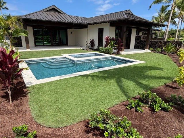 Modern home behind a swimming pool and raised spa, surrounded by a lawn and tropical landscaping.